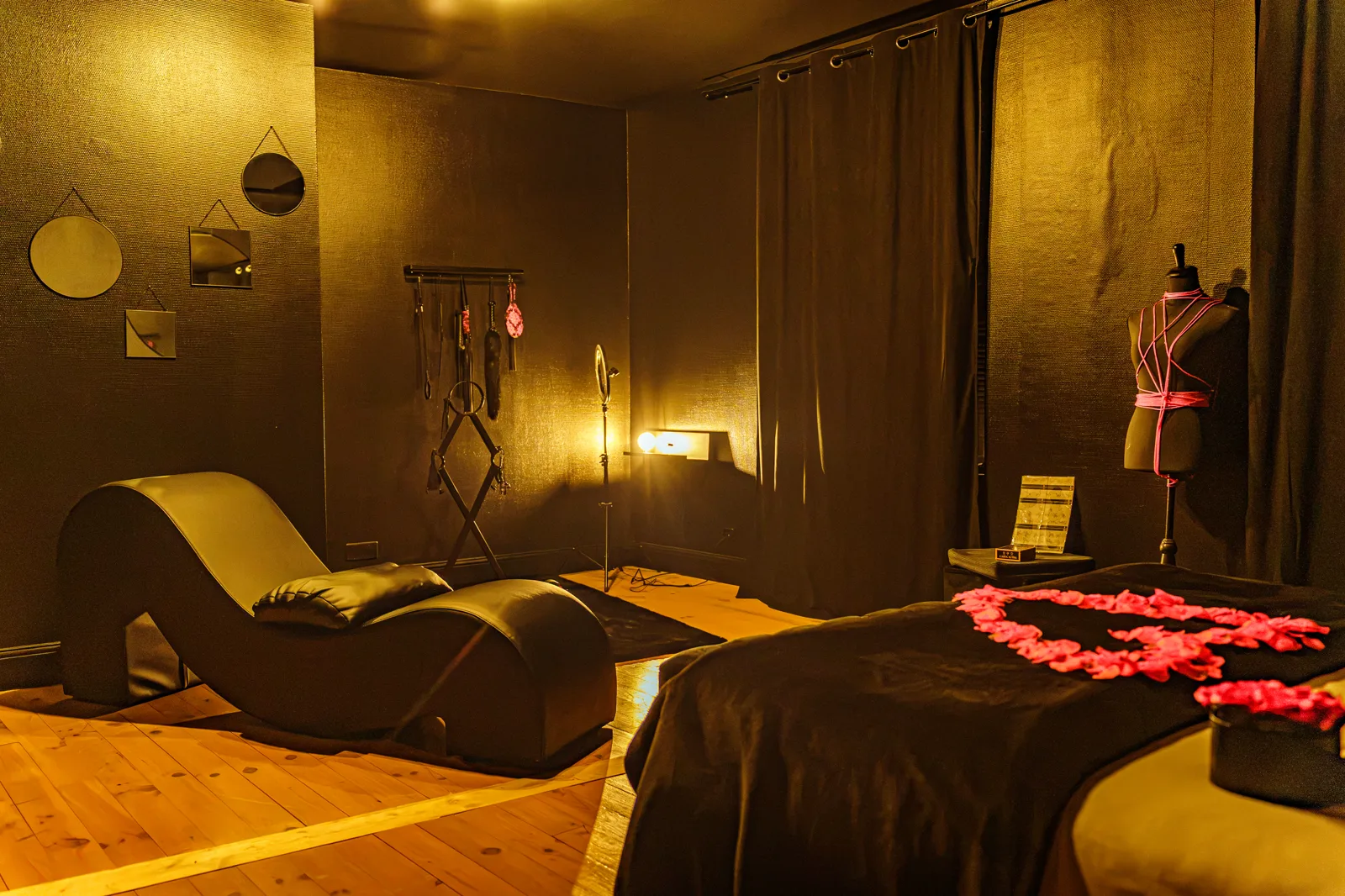 Le boudoir : accessoires suspendus au mur noir, bougies rouges et tapis moelleux