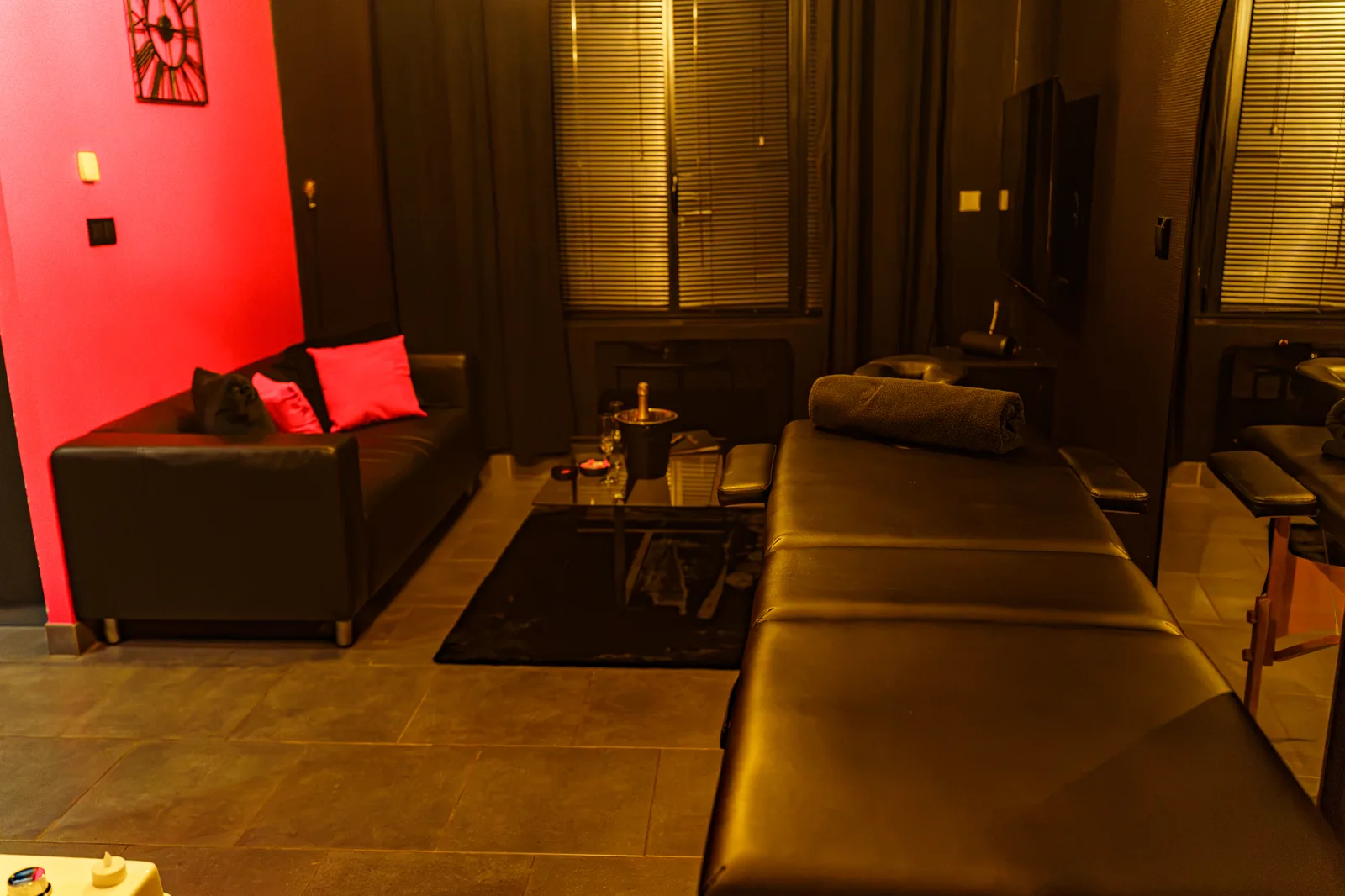 Le salon de La Maison Coquine : canapé noir, TV murale et chemin de pétales de roses rouges